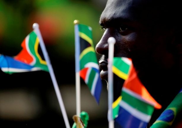 A man holds South African national flags as he stands in a queue at the Union Buildings in Pretoria December 12, 2013. Thousands of people lined the streets to view the body of  former South African President Nelson Mandela.   REUTERS/Kevin Coombs (SOUTH AFRICA - Tags: POLITICS OBITUARY SOCIETY) - RTX16EYF